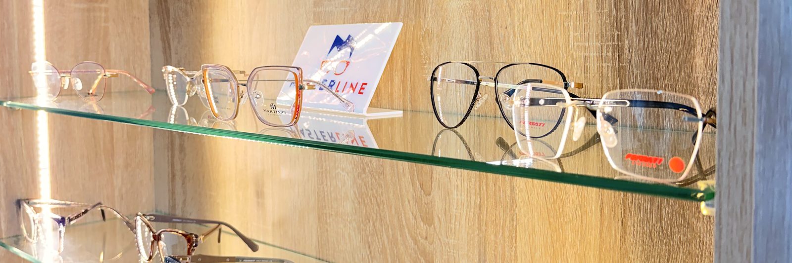 Exhibición de monturas en la óptica de Centro Ocular Gamavisión, en estantes de vidrio sobre madera clara